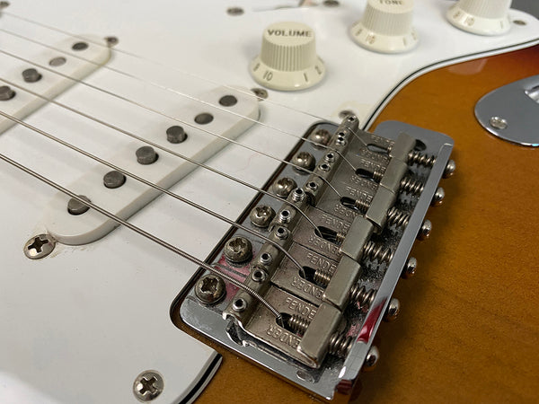 Close-up of Fender electric guitar chrome bridge, strings, white volume and tone knobs, and sunburst finish body