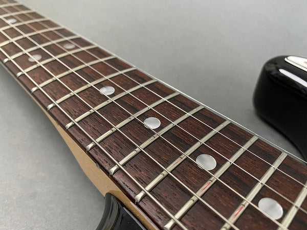 Close-up of electric guitar rosewood fretboard with dot inlays and metal frets, black guitar body edge visible on gray background