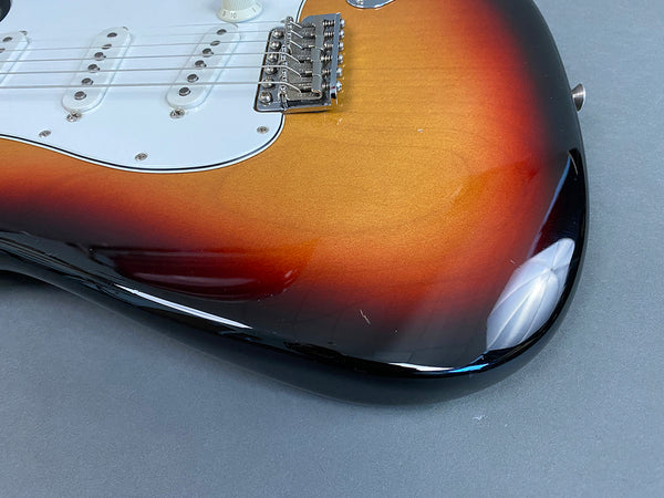 Close-up of sunburst electric guitar body showing white pickguard, pickups, bridge, and tone knob on grey background