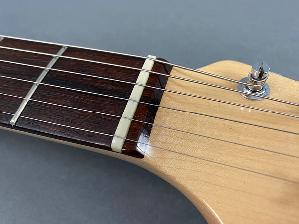 Close-up of guitar nut and fretboard showing steel strings and tuning peg on light wood headstock