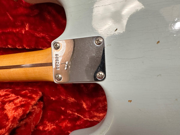 Close-up of guitar neck plate with serial number R9208 on a worn white electric guitar body resting on red plush fabric background