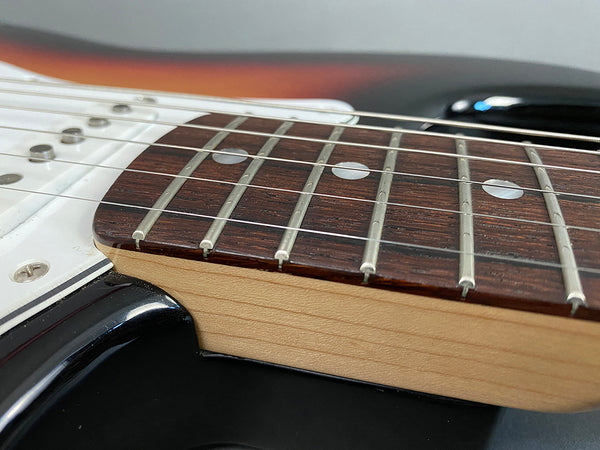 Close-up of electric guitar rosewood fretboard with dot inlays and maple neck on black body with white pickguard