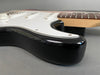 Close-up of black electric guitar body with white pickguard and maple neck on gray background