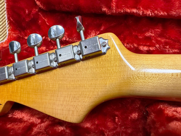 Close-up of guitar headstock with vintage chrome tuning pegs on natural wood finish neck resting on red plush case lining
