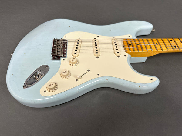 Light blue vintage electric guitar with white pickguard, three single-coil pickups, volume and tone knobs, and a maple neck with dot inlays on a gray background