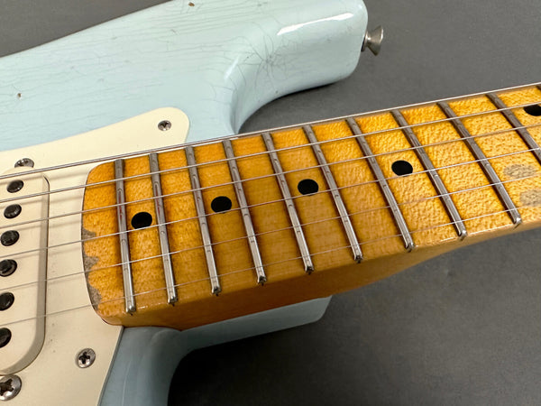 Close-up of vintage electric guitar maple neck and fretboard with worn frets and light blue body showing aging cracks and patina