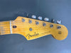 Close-up of vintage Fender Stratocaster guitar headstock with tuning pegs and strings, natural wood finish, original contour body text visible