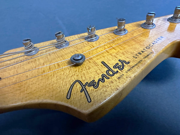 Close-up of natural wood Fender Stratocaster guitar headstock with tuning pegs and strings against dark background
