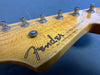Close-up of natural wood Fender Stratocaster guitar headstock with tuning pegs and strings on blue background