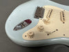 Close-up of vintage light blue electric guitar body showing chrome input jack, cream tone and volume knobs, cream pickguard, and single-coil pickups with aged finish and worn detailing.