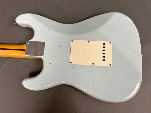 Back of light blue electric guitar body with cream plastic cover plate and bolt-on maple neck with red stripe, showing vintage wear and finish checking