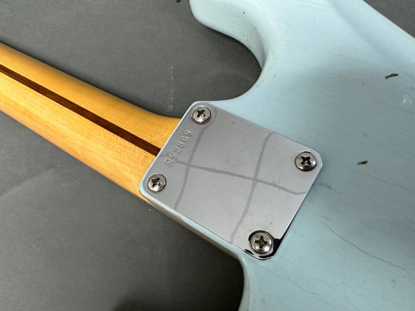 Close-up of guitar neck joint with chrome neck plate and serial number R92609 on light blue electric guitar body and natural wood neck with skunk stripe