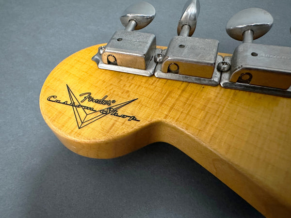 Close-up of Fender Custom Shop guitar headstock with vintage tuning pegs on a light maple wood finish against a gray background