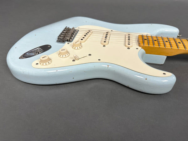 Light blue electric guitar body with white pickguard, three single-coil pickups, tone and volume knobs, and maple neck on gray background
