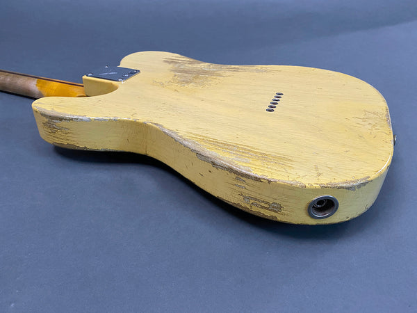 Back view of vintage yellow electric guitar with worn and chipped paint resting on gray surface
