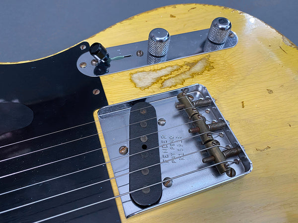 Close-up of vintage Fender guitar bridge and pickup on worn yellow body with black pickguard and chrome control knobs