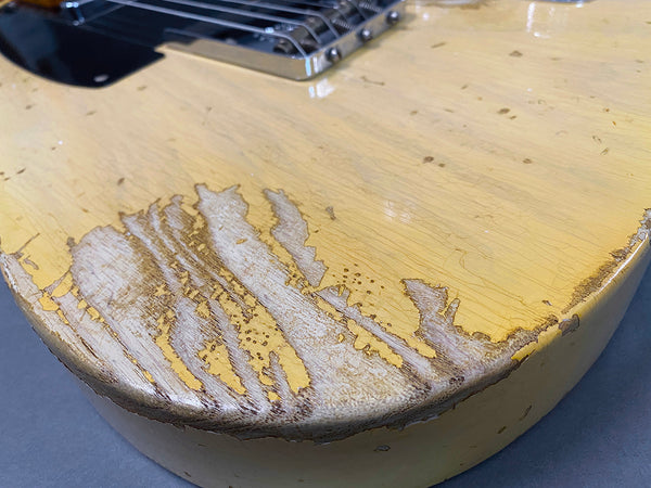 Close-up of worn yellow electric guitar body showing heavy finish wear and wood grain at the lower edge near the bridge.