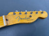 Close-up of vintage Fender Telecaster electric guitar headstock with tuning pegs and strings on grey background
