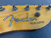 Close-up of Fender Telecaster guitar headstock with tuning pegs and strings on a natural wood finish background.