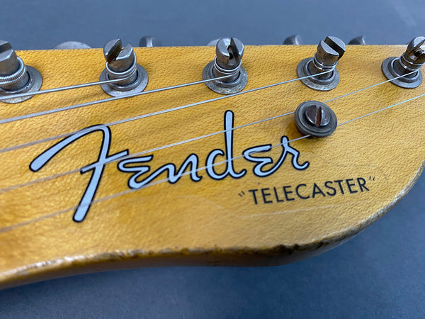Close-up of Fender Telecaster guitar headstock with tuning pegs and strings on a natural wood finish background.