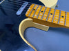 Close-up of vintage electric guitar neck with worn maple fretboard and black pickguard showing pickup and strings on gray background