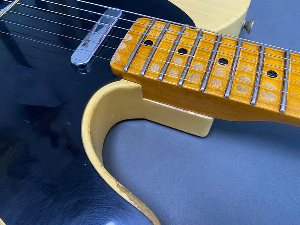 Close-up of vintage electric guitar neck with worn maple fretboard and black pickguard showing pickup and strings on gray background