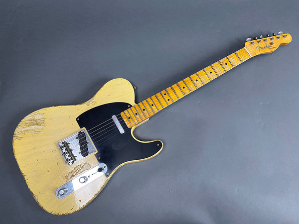 Vintage Fender Telecaster electric guitar with worn yellow finish and black pickguard on gray background