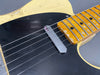 Close-up of vintage electric guitar body showing black pickguard, single chrome bridge pickup, worn yellow maple fretboard, and steel strings on a cream-colored guitar body