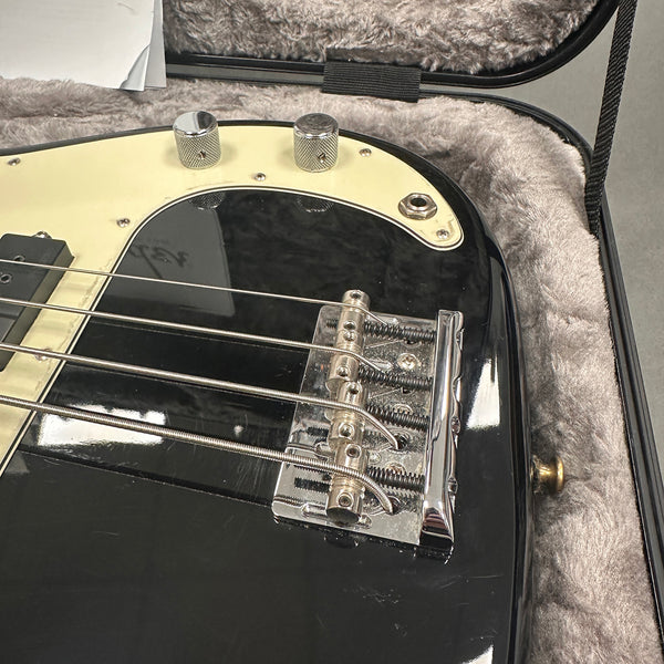 Close-up of black electric bass guitar bridge and control knobs with cream pickguard in plush guitar case