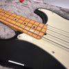 Close-up of black electric bass guitar with maple neck, white pickguard, and metal strings on gray plush background at Coffee House Guitars.