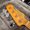 Close-up of Fender Precision Bass headstock with chrome tuning pegs and orange-wrapped bass strings resting in a grey plush guitar case interior.
