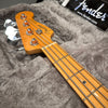 Fender Precision Bass guitar headstock and fretboard with chrome tuning pegs lying on a gray plush guitar case interior