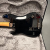 Back of black Fender electric guitar with maple neck resting in gray plush-lined hard case showing string ferrules and Fender neck plate