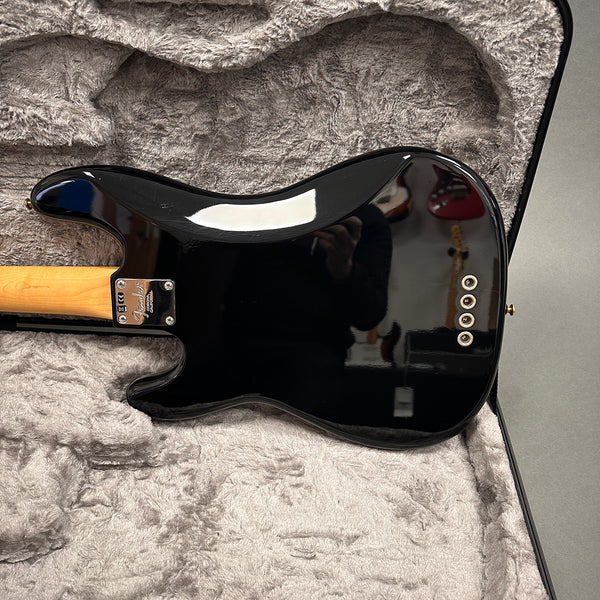 Back of black Fender electric guitar with maple neck resting in gray plush-lined hard case showing string ferrules and Fender neck plate