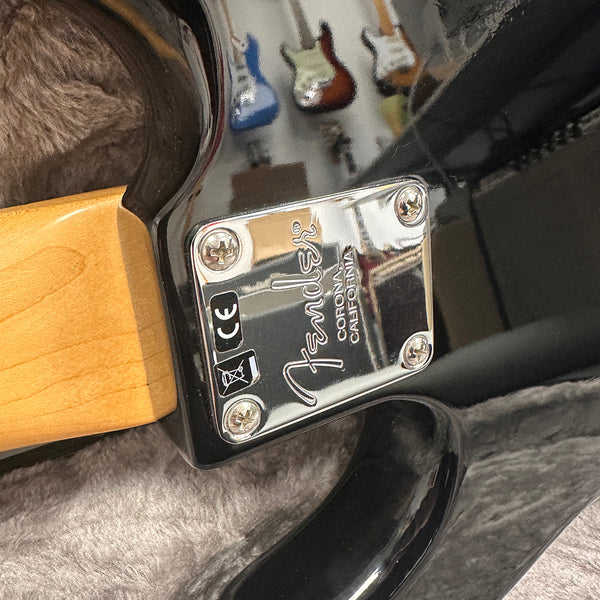 Close-up of Fender neck plate on black electric guitar with maple neck showing "Corona, California" engraving