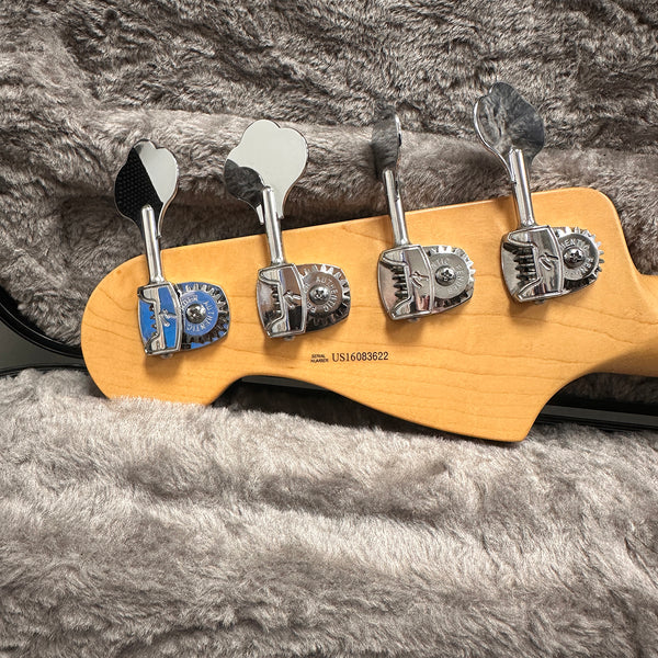 Close-up of maple bass guitar headstock with four chrome tuning pegs on plush gray guitar case lining