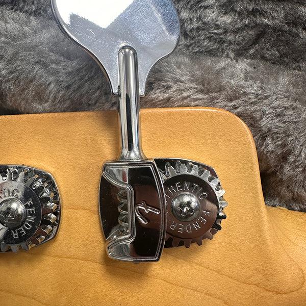 Close-up of Fender Authentic stamped chrome tuning peg on maple wood guitar headstock with plush gray background