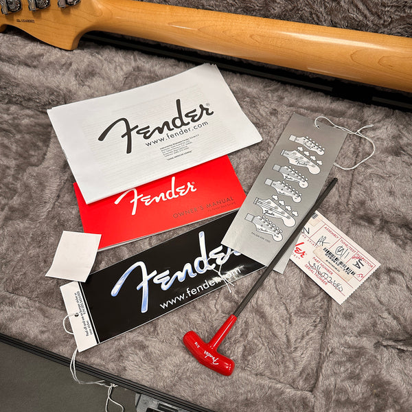 Fender guitar owner's manual, warranty card, product tags, and red Fender truss rod wrench on plush gray guitar case lining with guitar neck visible.