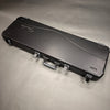 Black hard shell guitar case with silver latches and molded Fender logo on lid, shown closed on a gray surface.