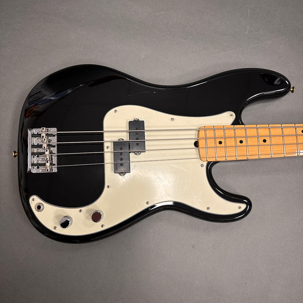 Black electric bass guitar with white pickguard and maple neck on gray background