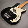 Black electric bass guitar with white pickguard and maple neck on gray background, showing strings, bridge, and control knobs close-up