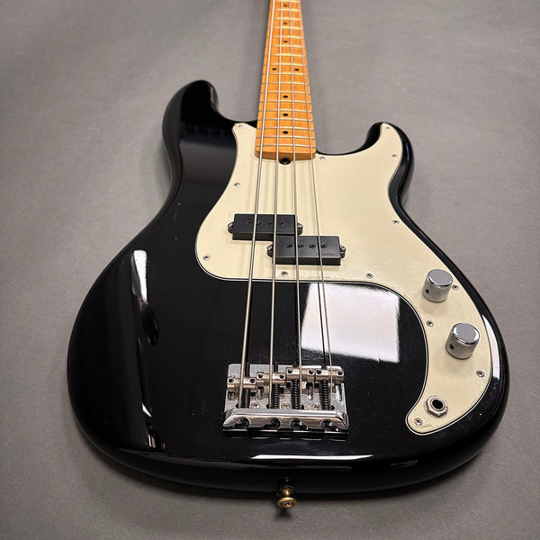 Black electric bass guitar with cream pickguard, maple neck, and chrome knobs and bridge on gray background