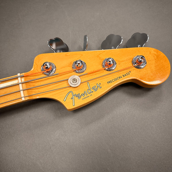 Close-up of Fender Precision Bass guitar headstock with tuning pegs and logo on natural wood finish background