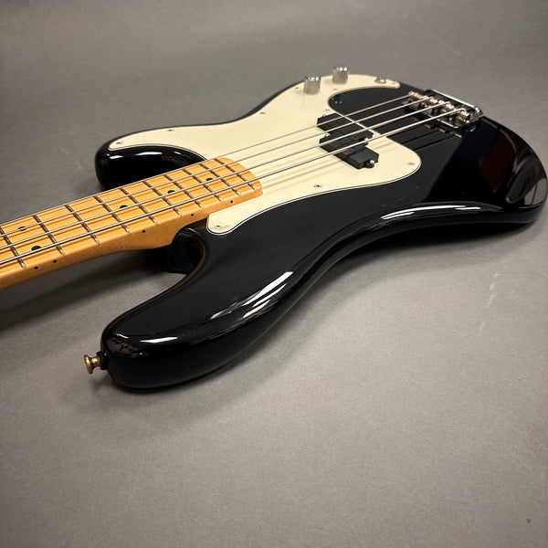 Black electric bass guitar with maple neck and white pickguard on gray background