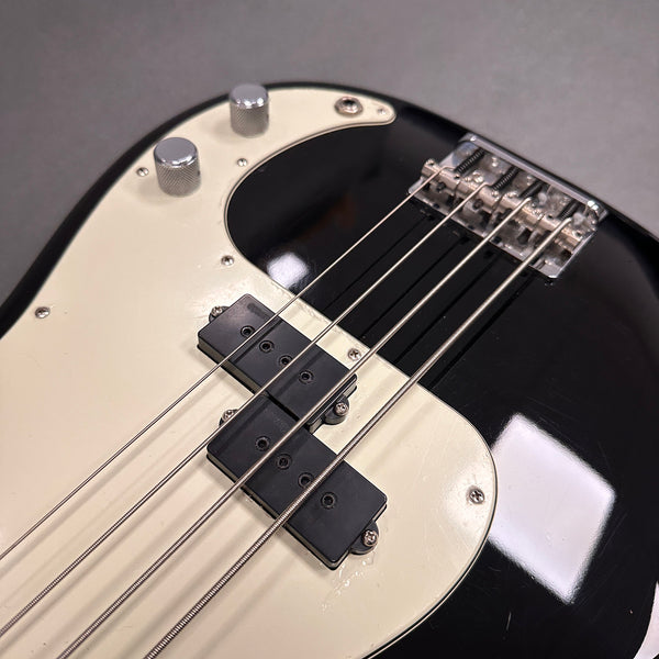 Close-up of black and white electric bass guitar body showing chrome control knobs, black pickups, and strings on white pickguard