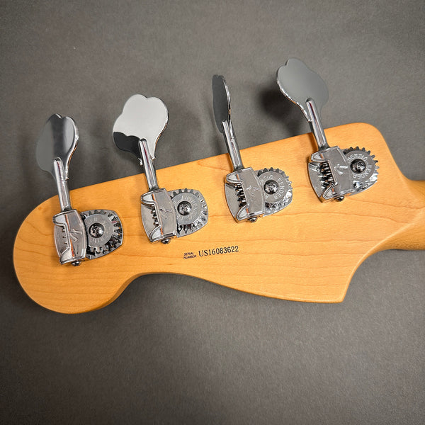Close-up of Fender bass guitar headstock with chrome tuning pegs and serial number US16083622 on natural maple wood background
