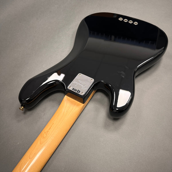 Back view of a black Fender electric guitar with a maple neck and metallic neck plate on gray background
