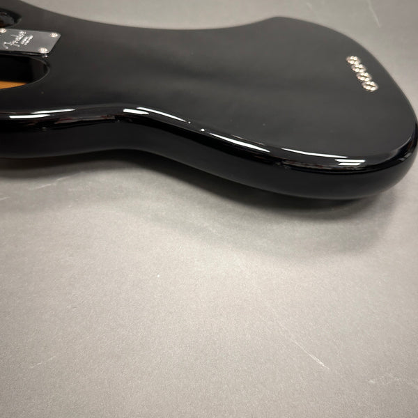 Close-up view of black glossy electric guitar body with contoured edge on gray surface