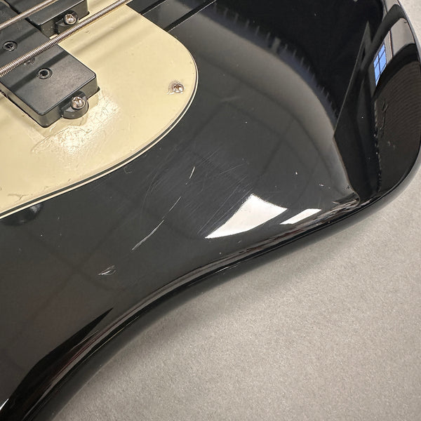 Close-up of black electric guitar body showing scratches and wear near cream-colored pickguard and pickups