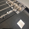 Close-up of black electric bass guitar bridge with metal saddles and strings showing surface scratches and wear